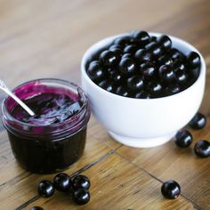 a bowl of blueberries next to a jar of blackberries on a wooden table