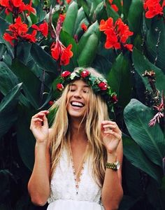 a woman wearing a flower crown standing in front of red flowers