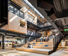 people are sitting on the stairs in an open area with large windows and wooden staircases