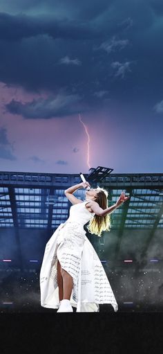 a woman in white dress standing on stage with lightning above her head and arm outstretched