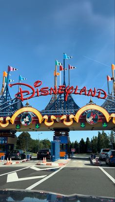 the entrance to disneyland land with flags flying in the wind and cars parked on the road