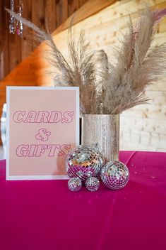 there is a card and some silver balls on the pink table cloth with feathers in it