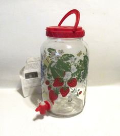 a glass jar with strawberries and flowers on it next to a red handled toothbrush