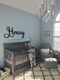 a baby's room with a gray crib, chair and chandelier