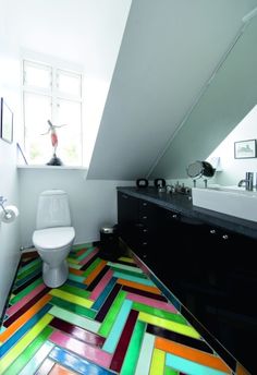 a bathroom with multicolored flooring and a white toilet next to a window