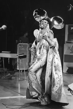 an old photo of a woman in costume on stage with other people behind her and one man standing next to her