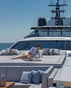 a woman laying on top of a couch next to a boat in the ocean and looking at her phone