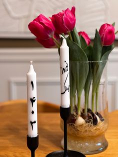 two candles are sitting on a table with flowers in the vase and one candle has writing on it