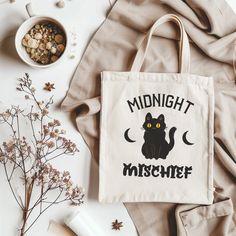 a black cat is sitting on top of a tote bag with the words midnight