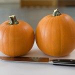 two pumpkins sitting on top of a cutting board next to a knife