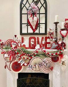 a mantel decorated with red and white decorations, including paper fan garlands, candles, and love signs