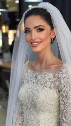 a woman in a wedding dress with a veil on her head and smiling at the camera