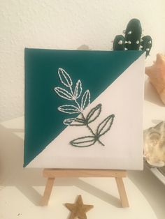 a small easel with a green and white painting on it next to seashells