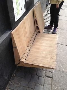 a wooden bench sitting on the side of a street next to a sidewalk with people walking by