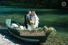 a bride and groom are standing in a boat on the river bank with just married sign