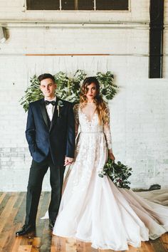 a man and woman standing next to each other in front of a white brick wall