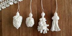 three white crocheted ornaments hanging from strings on a wooden table with doily