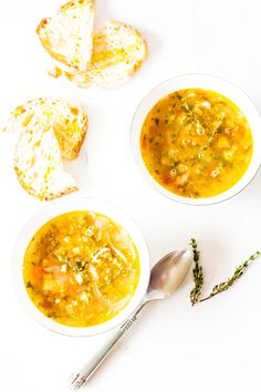 two bowls filled with soup next to slices of bread on top of a white table