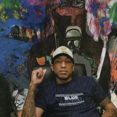 a man sitting in front of a wall covered with colorful paintings and writing on it