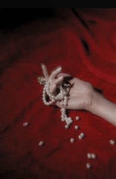 a woman's hand with beads on it laying on a red sheet and holding onto her fingers