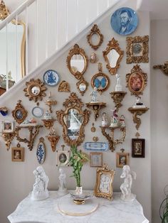 there is a wall with many different pictures and mirrors on it, along with a vase filled with flowers