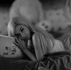 a black and white photo of a woman laying in bed with a book on her lap