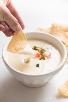 a person dipping tortilla chips into a bowl of quesadilla soup