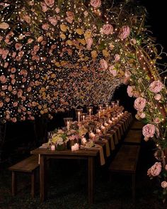 a long table covered in lots of flowers and lit candles with lights on the ceiling