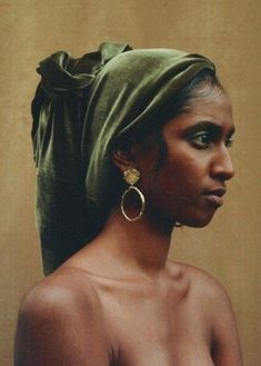 an african woman wearing large hoop earrings and a green scarf on top of her head