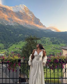 a woman standing on top of a balcony next to a lush green hillside covered in flowers