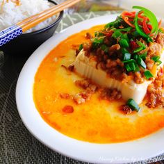 a white plate topped with food next to rice and chopsticks