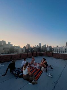 four people sitting on top of a roof eating pizza and drinking beer at sunset or dawn