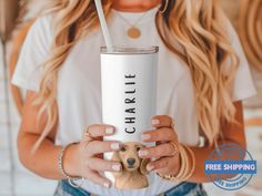 a woman holding a white coffee cup with a dog on the side and a straw in her hand