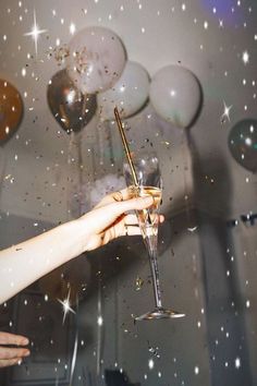 a person holding a wine glass in front of balloons and confetti on the wall