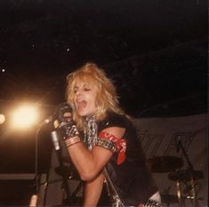 a woman singing into a microphone while holding a pair of gloves on her hand and standing in front of a stage