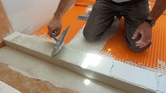 a man kneeling down on an orange floor with two pairs of scissors in his hand