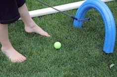 a person standing next to a blue and white tee ball on top of a green field