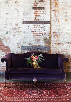 a purple couch sitting on top of a rug next to a brick wall and floor