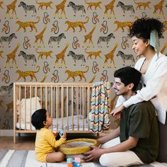 a woman and two children sitting on the floor in front of a wallpaper with giraffes