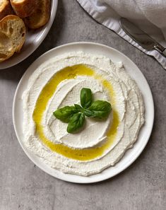 a white plate topped with hummus next to slices of bread on a gray table