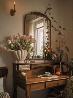 a wooden desk topped with a mirror next to a vase filled with flowers and candles