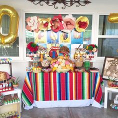 a colorful table topped with lots of desserts and balloons in front of a window