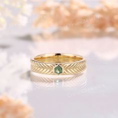 a gold ring with a green stone in the center on a white table next to flowers