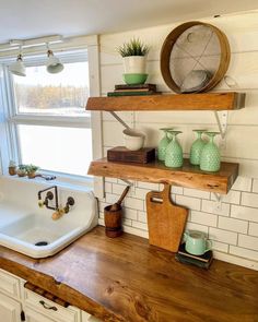 a bath tub sitting under a window next to a wooden shelf filled with vases