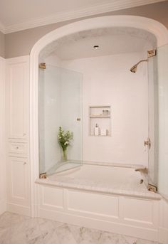 a white bathroom with marble flooring and an arched shower door that leads to the bathtub