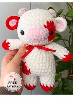 a crocheted teddy bear is being held by a person's hand with a plant in the background