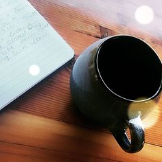 a laptop computer sitting on top of a wooden table next to a coffee cup and pen