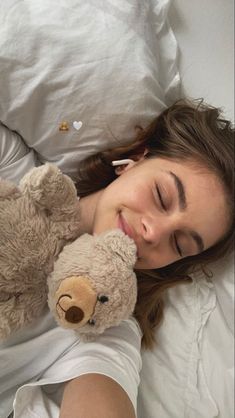 a woman laying in bed with her eyes closed and holding a teddy bear up to her face