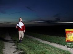 a man walking down a dirt road at night with a bag of corn on the side