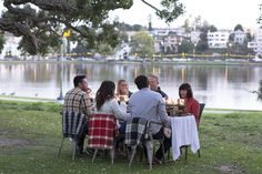 a group of people sitting at a table in front of a body of water eating food